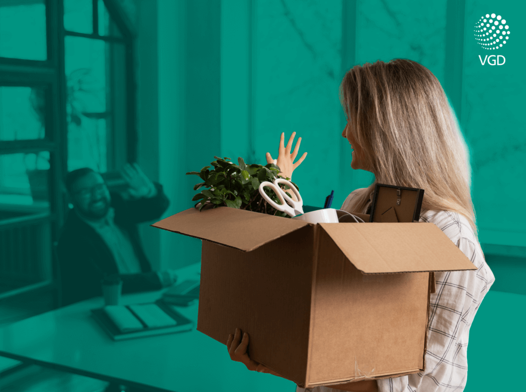 a smiling woman holds a box with office supplies in her hand and with her other hand she waves goodbye to a man in the office