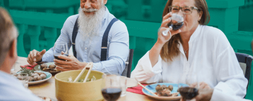 an elegant senior man with a gray beard sits at a table with other people during a business lunch