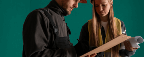 A man and a woman are at the construction site, looking at documents.